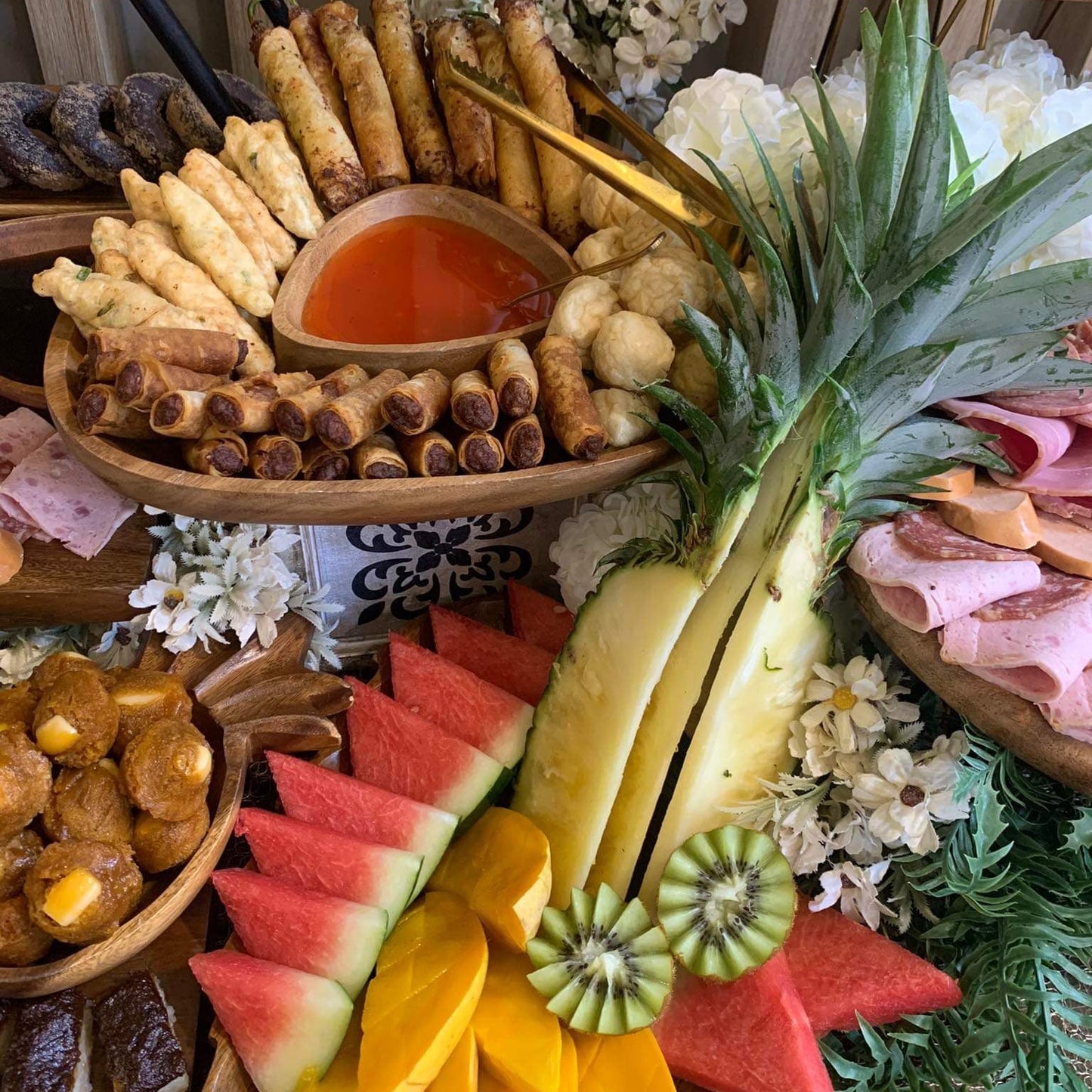 Assorted fruits and meats on a platter with decorative flowers.